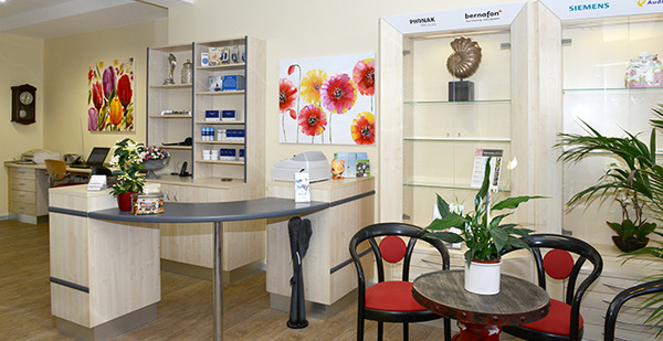 Modernes Hörakustik-Fachgeschäft mit Empfangstresen, Pflanzen und farbiger Wanddekoration.